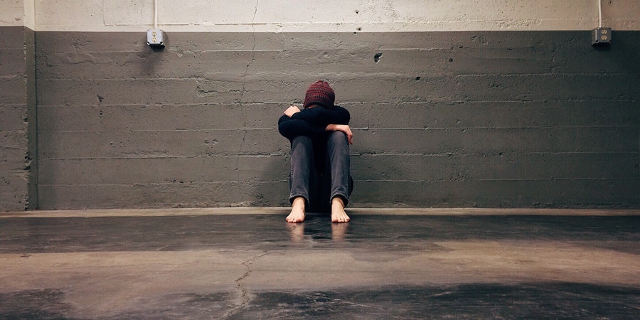 a visibly stressed woman sitting on concrete floors with a brick wall in a dark room